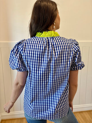 Woman wearing a blue and white checkered blouse with green trim in a room.
