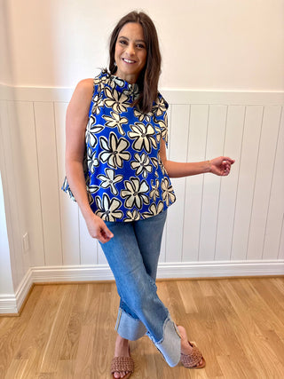 Woman wearing a blue floral sleeveless top and jeans indoors.