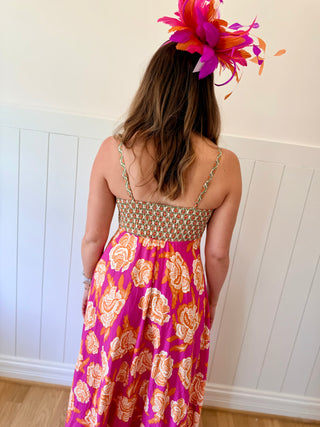 Person wearing a colorful dress with floral patterns and a vibrant headpiece against a white paneled wall.