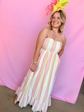 Woman in a striped dress with a colorful headpiece against a pink background
