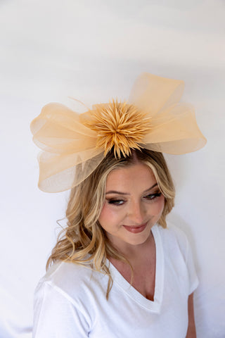 Woman wearing a large beige bow headpiece against a white background