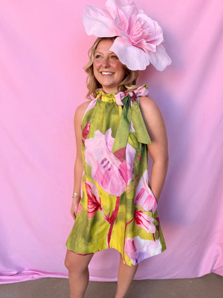 Woman wearing a floral dress and large hat against a pink background