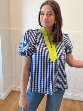 Woman wearing a blue and white checkered top with a yellow accent indoors.