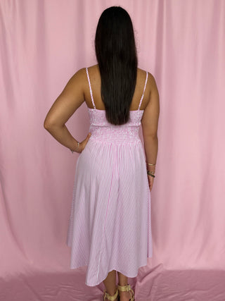 Woman wearing a white and blue striped dress against a pink curtain background
