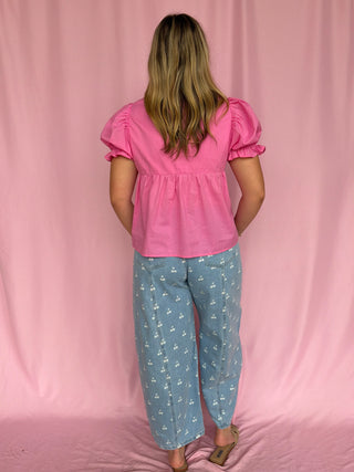Woman wearing a pink top and blue floral pants against a pink curtain background