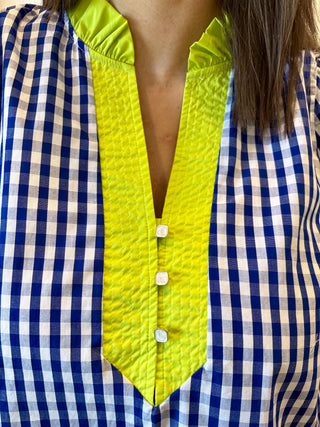 Close-up of a blue and white checkered shirt with a bright yellow vest over it.