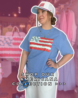 Person wearing a blue t-shirt with an American flag design and a cap, standing in a store with pink clothing in the background.