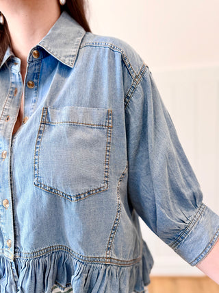 Close-up of a person wearing a light blue denim shirt with a plain background