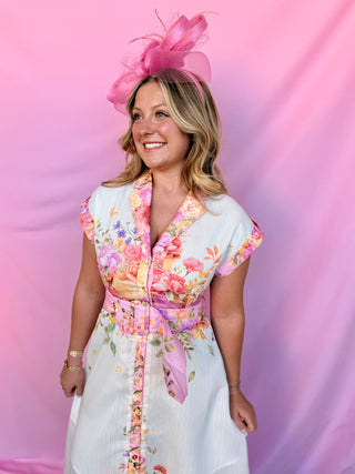 Woman wearing a floral dress with a pink hat against a pink background