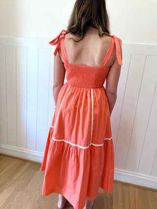 Woman wearing a coral dress with thin straps in a room with white paneled walls.