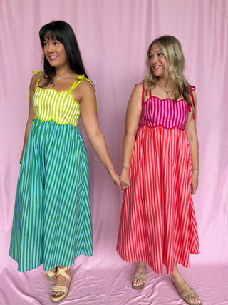 Two women wearing colorful striped dresses against a pink background