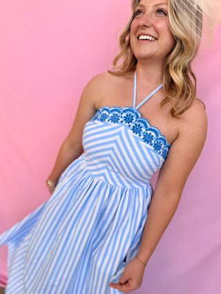 Woman wearing a blue and white striped dress with floral details against a pink background