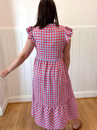 Person wearing a red and white checkered dress in a room with wooden flooring and white walls.