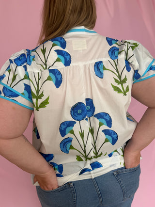 Person wearing a white blouse with blue floral patterns on a pink background