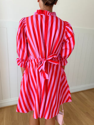 Person wearing a red and pink striped dress against a white wall.