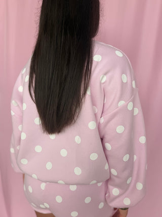 Person wearing a pink polka dot outfit against a pink curtain background