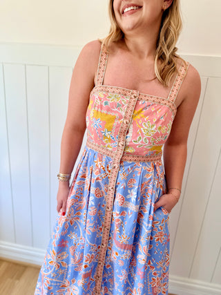 Woman wearing a colorful floral dress against a white paneled wall.