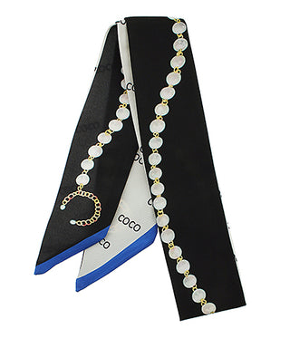 Black scarf with a white and blue pattern draped over a black background, featuring a necklace with white beads and gold accents.