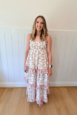 Woman wearing a floral dress and pink fascinator against a white paneled wall.