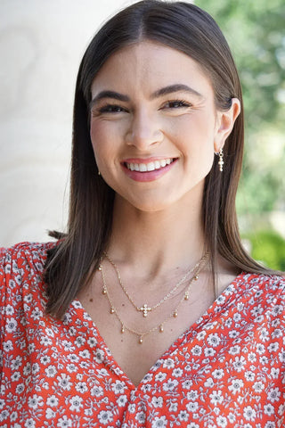Woman wearing gold necklaces and earrings with a blurred outdoor background