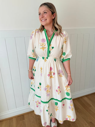 Woman wearing a floral dress standing against a white paneled wall.