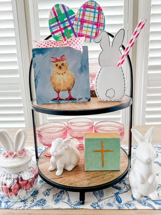 Decorative items on a tiered stand with Easter theme, including a chick painting and bunny figures.