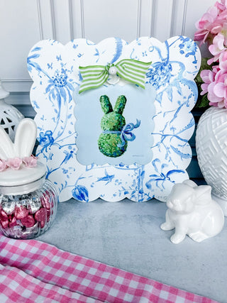 Decorative frame with a green bunny design on a table with decorative items.