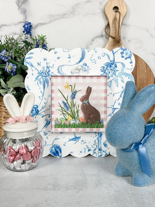 Decorative Easter scene with a framed picture, candy jar, and plush bunny on a marble surface.