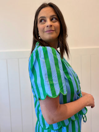 Woman wearing a green and blue striped dress against a white wall.