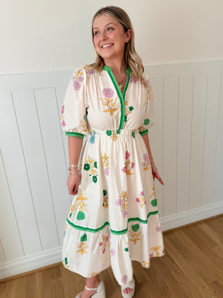 Woman wearing a floral dress standing against a white paneled wall.