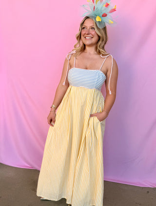 Woman wearing a striped dress and colorful headpiece against a pink background