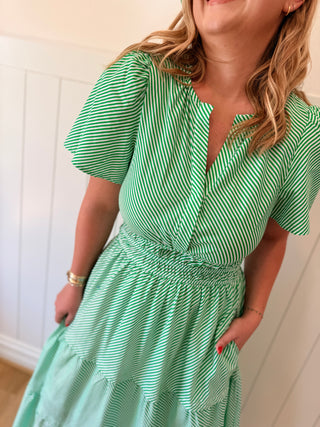 Woman wearing a green and white striped dress against a white wall.