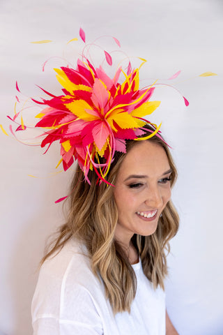 Woman wearing a vibrant pink and yellow feathered headpiece against a white background