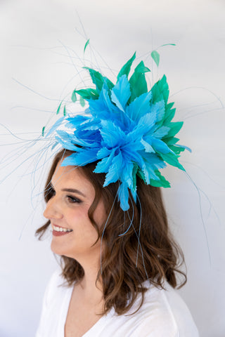 Woman wearing a blue and green feathered headpiece against a white background