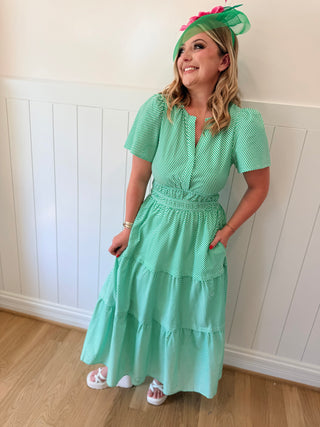 Woman wearing a green dress and matching hat against a white paneled wall.
