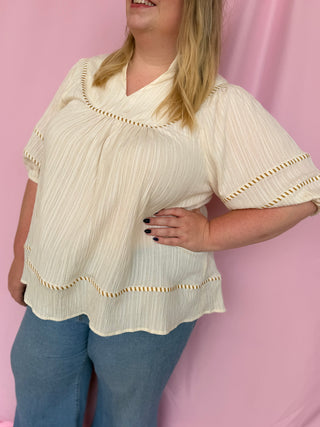 Woman wearing a beige blouse with white trim against a pink background