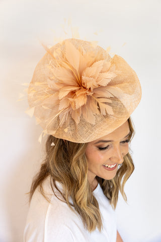 Woman wearing a peach-colored fascinator hat against a white background