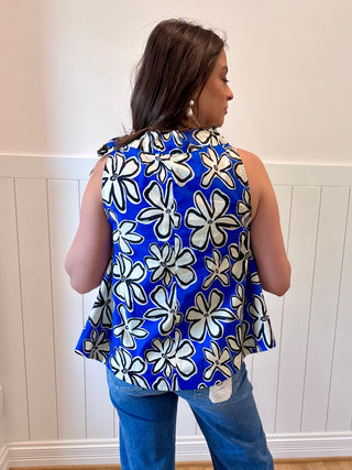 Woman wearing a blue sleeveless top with white floral pattern against a white wall.