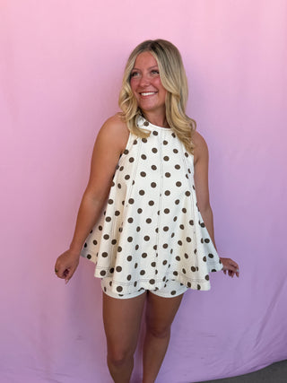 Woman wearing a white dress with brown polka dots against a pink background