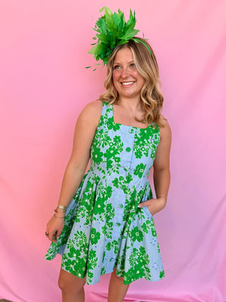 Woman wearing a green and blue floral dress with a large green headpiece against a pink background