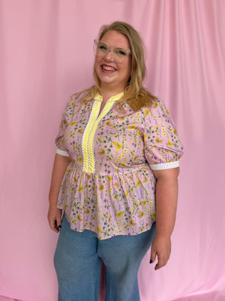 Woman wearing a floral blouse with yellow accents against a pink background