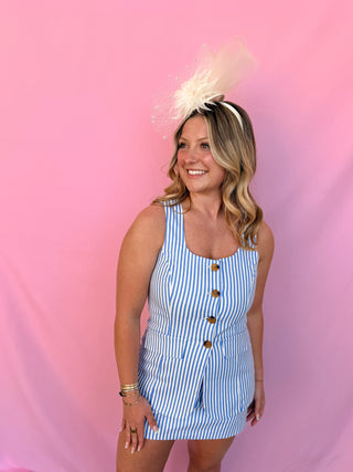 Woman wearing a blue and white striped dress with a feathered headband against a pink background