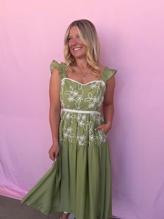 Woman wearing a green dress with white floral embroidery against a pink background