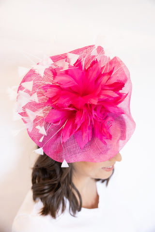Woman wearing a bright pink fascinator hat on a white background
