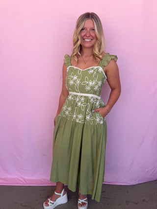 Woman wearing a green dress with white floral embroidery against a pink background