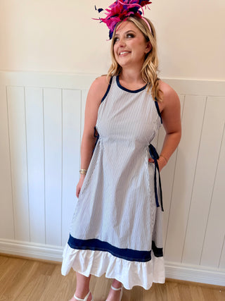 Woman wearing a white and blue striped dress with a decorative headpiece against a white paneled wall.