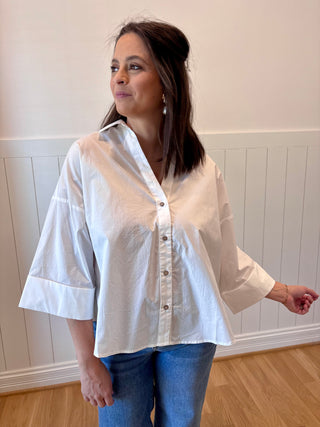 Woman wearing a white blouse with bell sleeves in a room with white paneled walls.