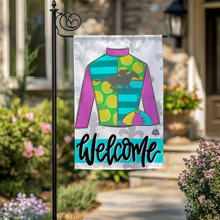 Decorative garden flag with colorful jockey silhouette and 'Welcome' text, displayed outdoors.