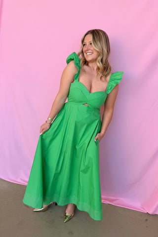 Woman in a green dress with ruffled sleeves and a floral headpiece against a pink background