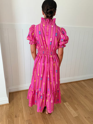 Person wearing a pink dress with floral patterns standing in a room with wooden flooring and white walls.